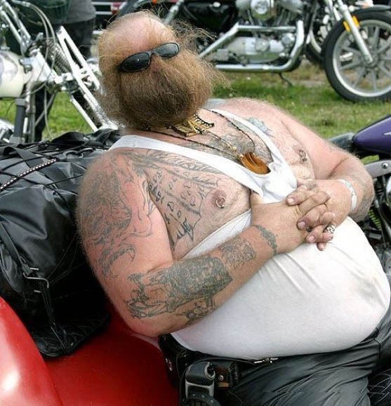 Qu'y a-t-il de plus affreux sur ce bien biker barbu ? Sa barbe, son marcel, ses tatouages ou ses percings sur ses tétons ? height=